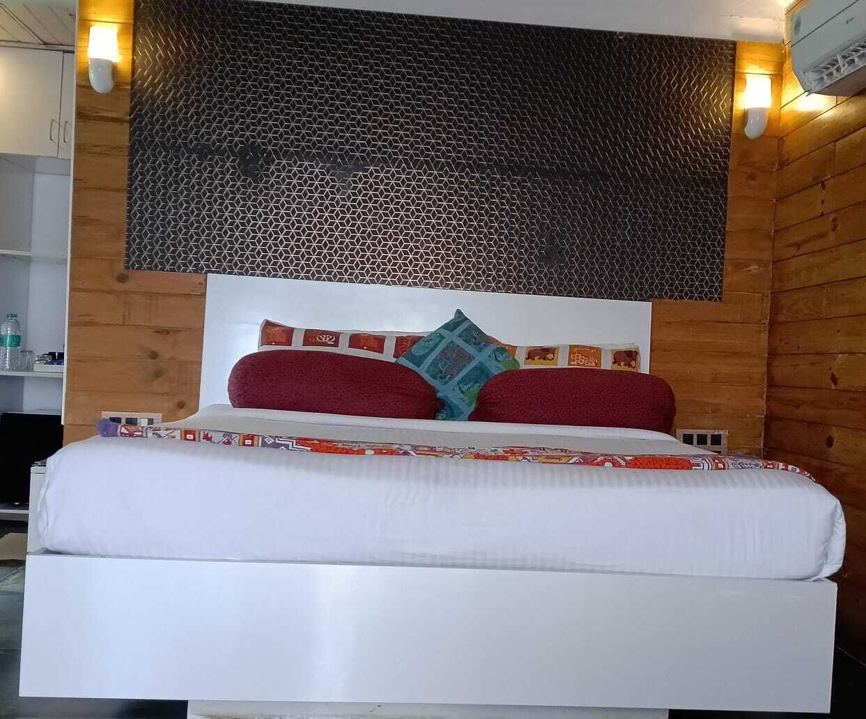 A bed with white bedding, red and blue pillows, and a patterned headboard.