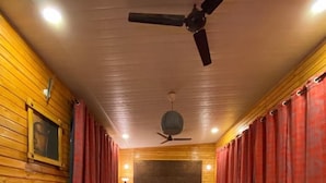 A compact room with a bed, two black sofas, a small round table, and a ceiling fan. - Rumourss Sky Villa (Lonavala)