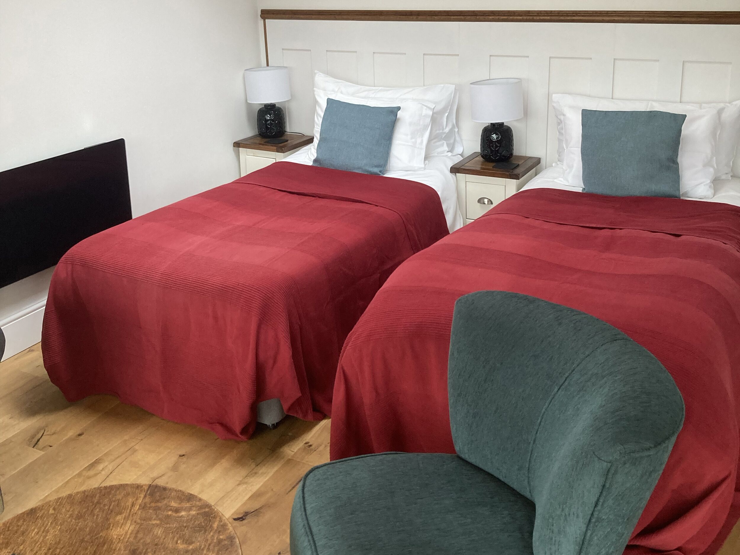 Ein Hotelzimmer mit zwei Betten, jeweils mit roter Bettdecke und weißen Kissen. Zwei Nachttische mit Lampen und ein Holz-Kopfteil sind vorhanden.