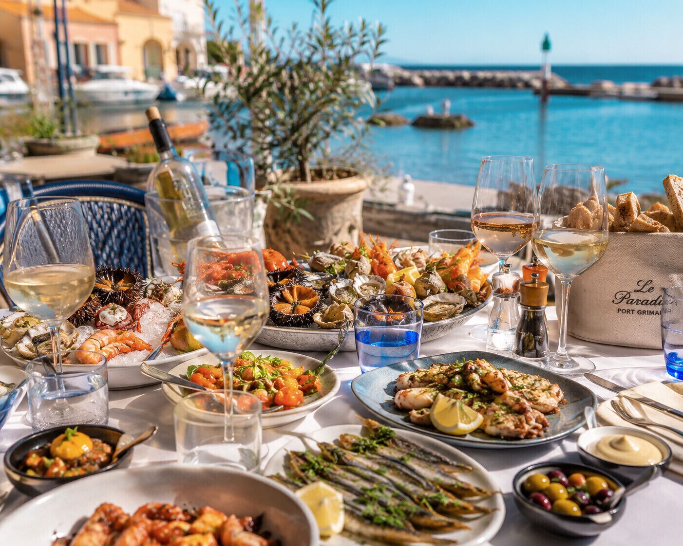 Una mesa servida con platos de mariscos, copas de vino blanco y vistas al mar.