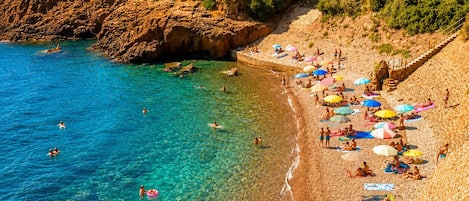 Une plage à l’eau claire, où l’on peut voir des gens nager et bronzer, avec une falaise rocheuse en arrière-plan.
