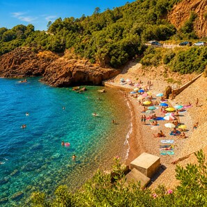 A beach with clear water, people swimming and sunbathing, and a rocky cliff in the background. - Provencal Villa with private pool large garden - Villa du Vallon by Sur la mer (Saint Raphael)