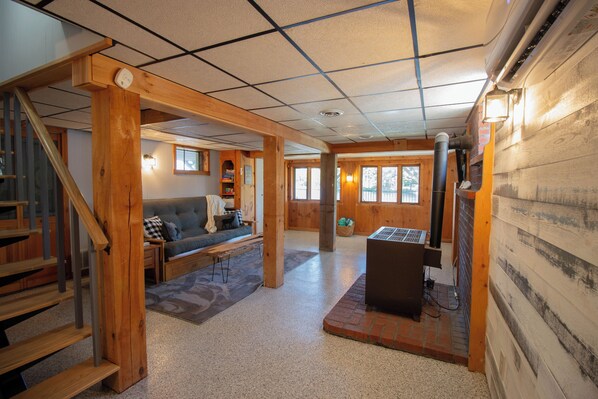 A spacious living area with a wooden staircase, a sofa, a fireplace, and a large window. - Lakefront Home w/ Private Dock & Water Access (Shapleigh)