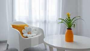 A white chair with a yellow cushion and a white pillow with a flower design, a white table with an orange vase, and a plant. - Welcome to Homiday Yellow Submarine, a modern, fully renovated apartment just a 10-minute walk from the Viareggio seafront. Bright and welcoming, it features a double bedroom, a comfortable sofa bed, a fully equipped kitchen, air conditioning, a washing  (Viareggio)