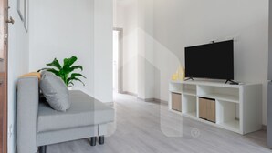 A modern living room with a grey sofa, a flat-screen TV on a white stand, a potted plant, and a staircase leading to another level. - Welcome to Homiday Yellow Submarine, a modern, fully renovated apartment just a 10-minute walk from the Viareggio seafront. Bright and welcoming, it features a double bedroom, a comfortable sofa bed, a fully equipped kitchen, air conditioning, a washing  (Viareggio)