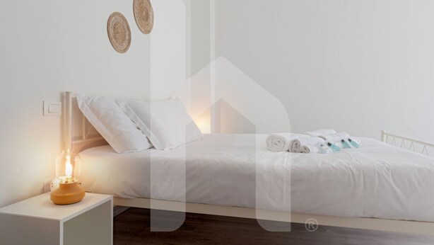 A neatly made bed with white linens, a bedside lamp, and a small table with towels and toiletries. - Welcome to Homiday Yellow Submarine, a modern, fully renovated apartment just a 10-minute walk from the Viareggio seafront. Bright and welcoming, it features a double bedroom, a comfortable sofa bed, a fully equipped kitchen, air conditioning, a washing  (Viareggio)