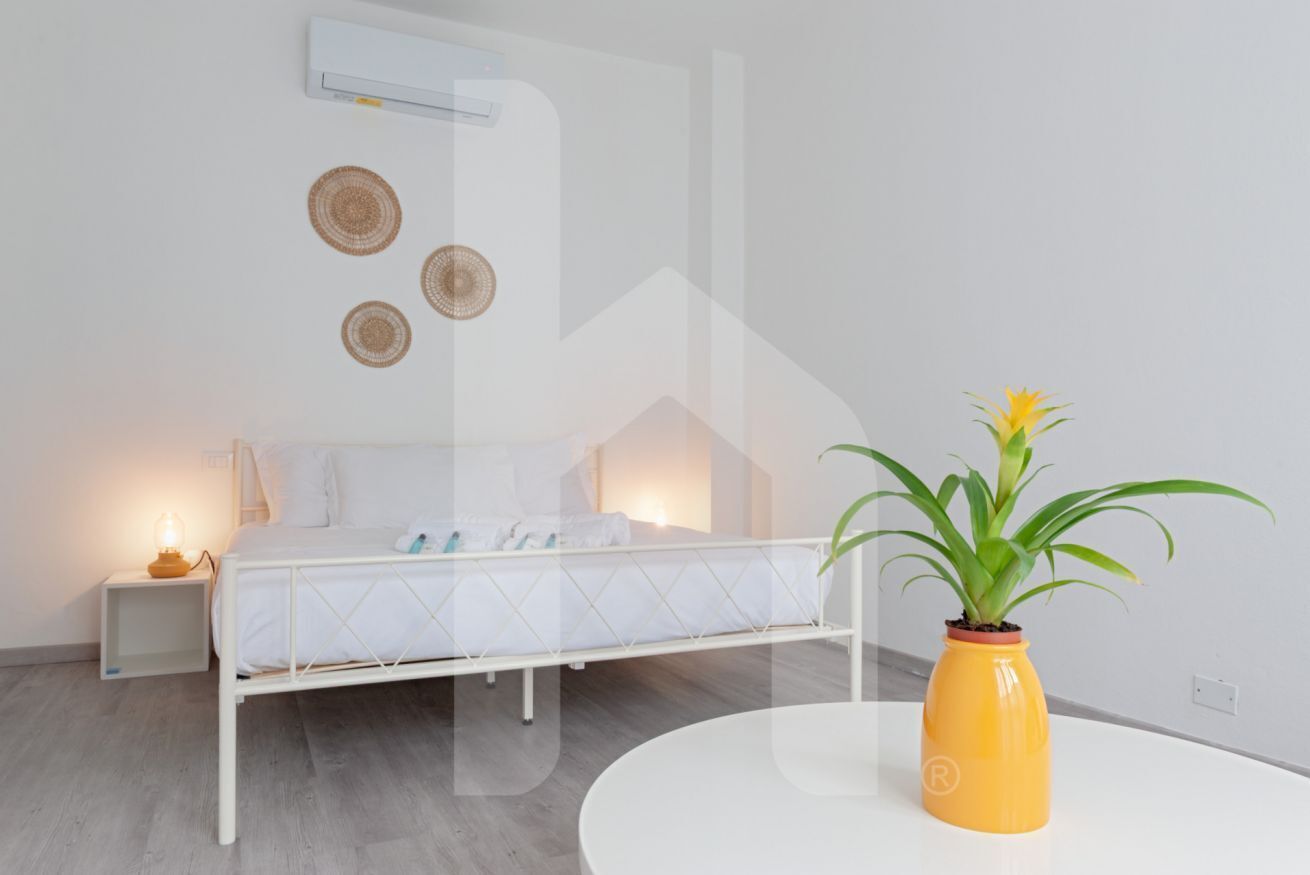 A bedroom with a bed, bedside table, and a potted plant.