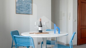A round table with a bottle of wine, two glasses, and a wooden coaster. Four blue chairs surround the table. - Welcome to Homiday Yellow Submarine, a modern, fully renovated apartment just a 10-minute walk from the Viareggio seafront. Bright and welcoming, it features a double bedroom, a comfortable sofa bed, a fully equipped kitchen, air conditioning, a washing  (Viareggio)