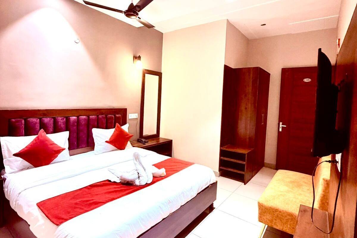 A hotel room with a large bed, a ceiling fan, a mirror, a TV, and a small seating area.
