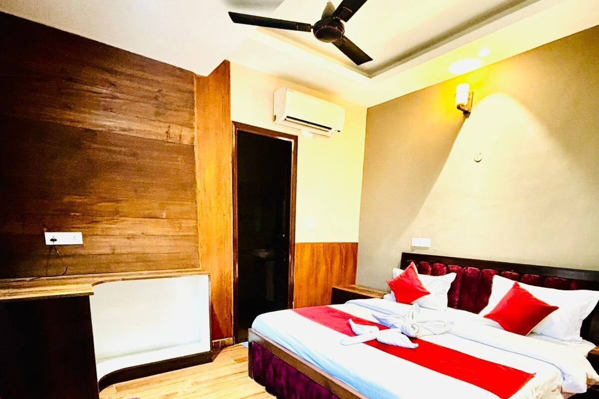 A bedroom with a wooden floor, a bed with red and white bedding, a ceiling fan, and an air conditioning unit.