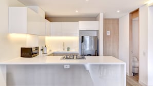 A modern kitchen with white cabinetry, a stainless steel refrigerator, and a central island with a built-in stove. - w Colorful Loft w Balcony in Santa B Rbara (Bogotá)