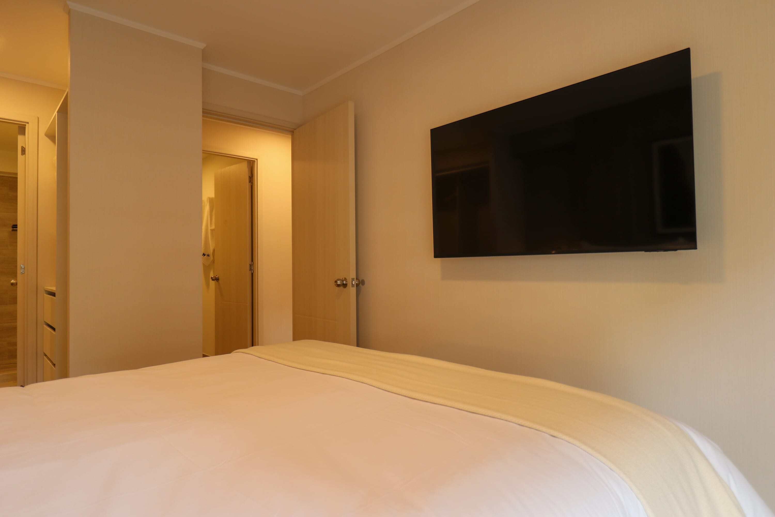 A hotel room with a bed, a television mounted on the wall, and a door leading to another room.