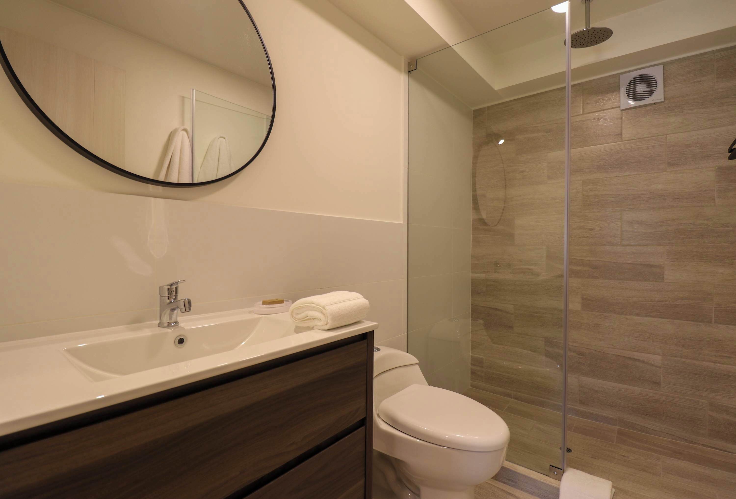 Un baño moderno con un espejo grande, un lavamanos, un inodoro y una zona de ducha con mampara de vidrio.