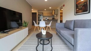 Un salon moderne doté d’un téléviseur à écran plat, d’un canapé gris et d’un coin repas avec une table et des chaises blanches.