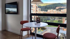 A modern room with a round table, two chairs, a TV mounted on the wall, and a large window offering a view of a cityscape and hills. - w Amazing Loft in the Heart of Bogot (Bogotá)