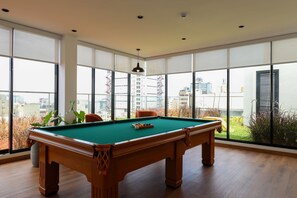 Uma mesa de bilhar em um ambiente com grandes janelas e vista para edifícios.