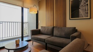 En moderne stue med sofa, et rundt bord og et stort vindue med udsigt til bygninger.