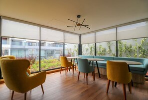 Um interior moderno com janelas amplas, um sofá verde, cadeiras amarelas e piso de madeira.