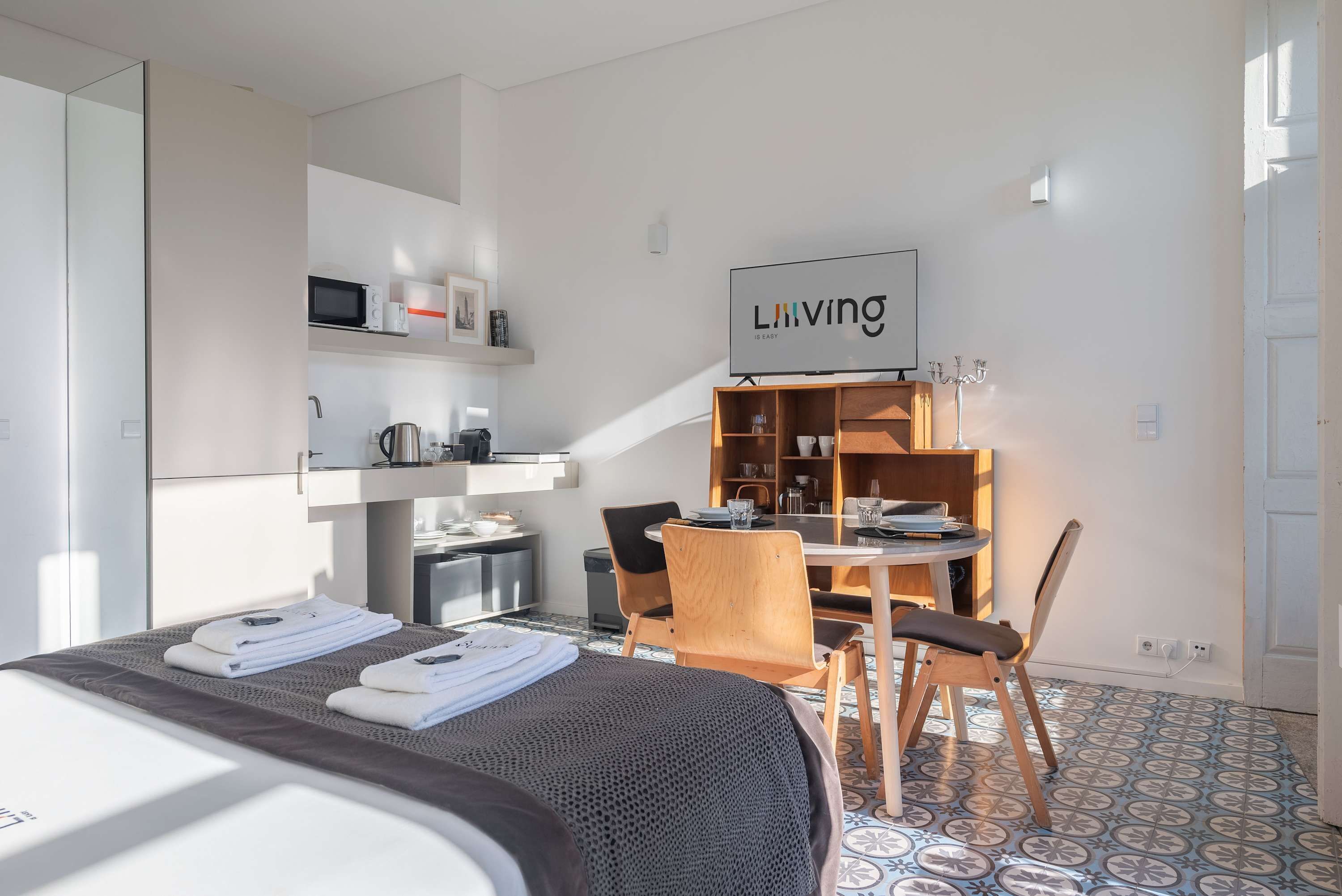 A hotel room with a bed, a dining table with chairs, a kitchen area, and a sign that says 'Living is Easy'.