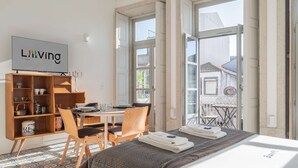 A hotel room with a bed, a TV, a wooden cabinet, a dining table, chairs, and a balcony with a view. - Liiiving in Porto - Design Palace Studio (Porto)