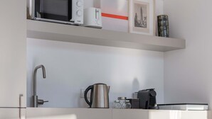 A compact kitchenette with a microwave, kettle, and coffee maker on a shelf, a sink, and a patterned floor. - Liiiving in Porto - Design Palace Studio (Porto)
