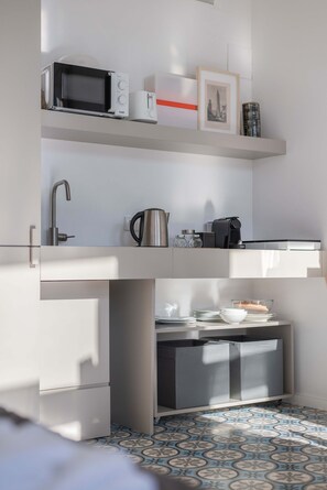 Une petite cuisine équipée comprenant un micro-ondes, une bouilloire et une machine à café placés sur une étagère, un évier et un sol à motifs.