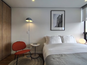 A modern hotel room with a bed, a red chair, a floor lamp, a small table, and a framed picture on the wall. - w Dreamlike Loft in the Heart of Bogot (Bogotá)
