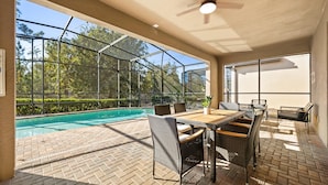A covered outdoor area with a pool, wicker furniture, and a view of trees. - Upstay Epic Windsor Home w Pool Cinema Games (Kissimmee)
