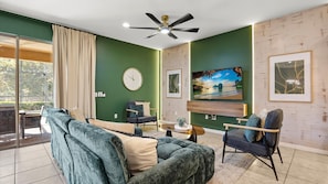 Un salon moderne avec un canapé, des fauteuils, un téléviseur et un ventilateur de plafond.