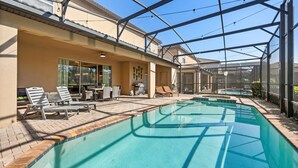 A covered outdoor swimming pool with lounge chairs and a table, surrounded by a glass enclosure. - Upstay Epic Windsor Home w Pool Cinema Games (Kissimmee)