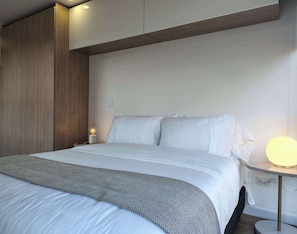 A modern hotel room with a large bed, a bedside table with a lamp, and a wall-mounted shelf. - w Enchanting Loft in the Heart of Bogot (Bogotá)