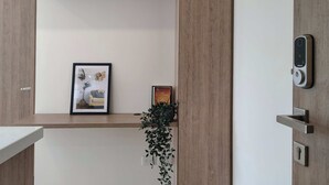 Une chambre moderne avec une porte en bois, un tableau encadré au mur, une petite plante et une serrure numérique sur la porte.