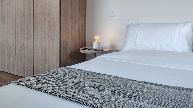 Une chambre à coucher moderne avec un grand lit, une table de chevet avec une lampe et un mur recouvert de panneaux en bois.
