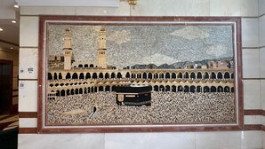 A large mosaic mural depicting a mosque with a minaret and a Kaaba, framed in a wooden border, set against a marble wall in a lobby area. - Grand Jawaher Alhashmiye Hotel Makkah (Makkah)