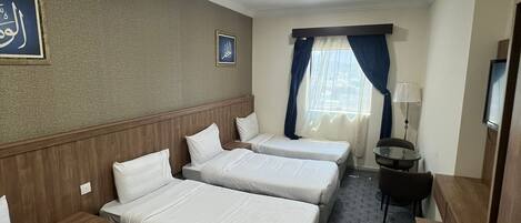 Una habitación de hotel con tres camas individuales, una mesita pequeña, una lámpara y un televisor.