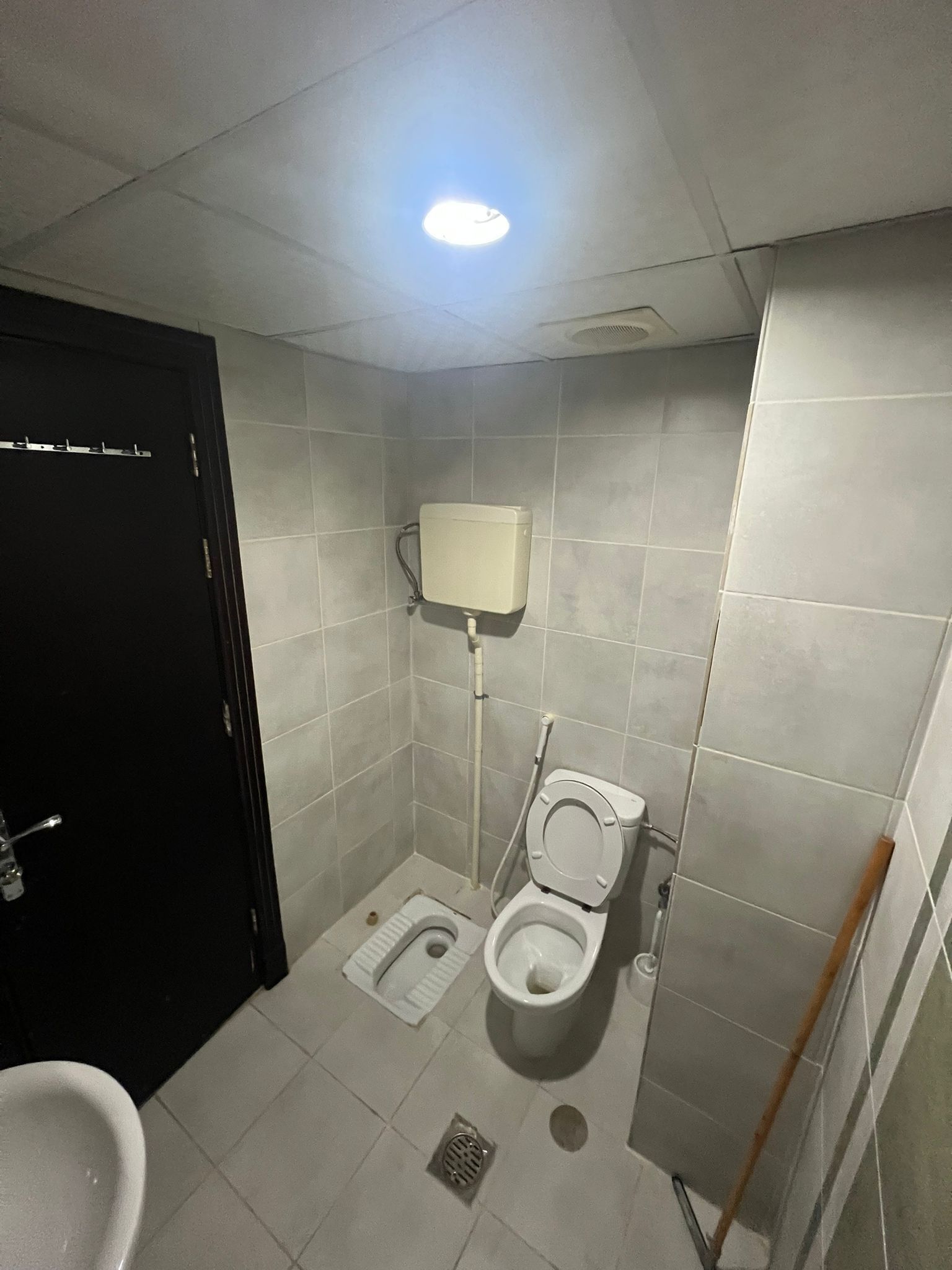 A small, tiled bathroom with a toilet, bidet, and a black door.