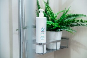 A bathroom shelf with a white bottle labeled "Reduce Respect Protect" and a potted fern. - The Art House (Cernobbio)