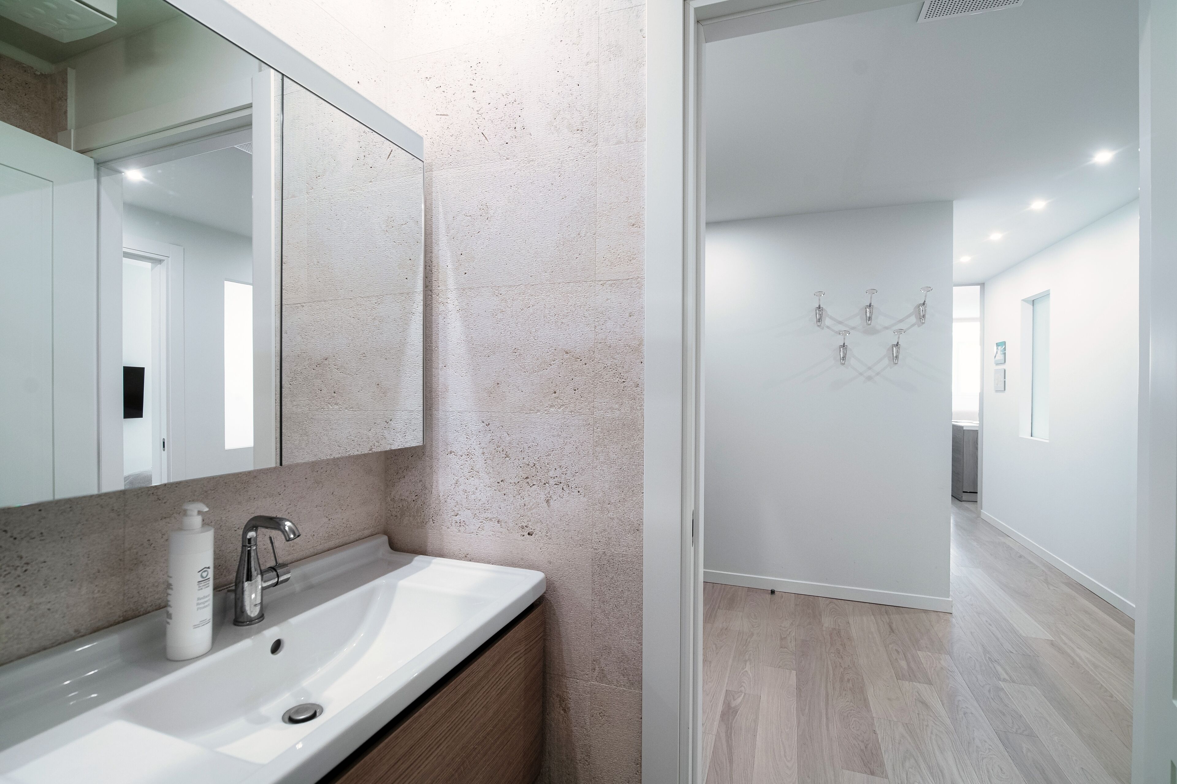 Un baño moderno con un espejo grande, lavamanos blanco y tocador de madera.