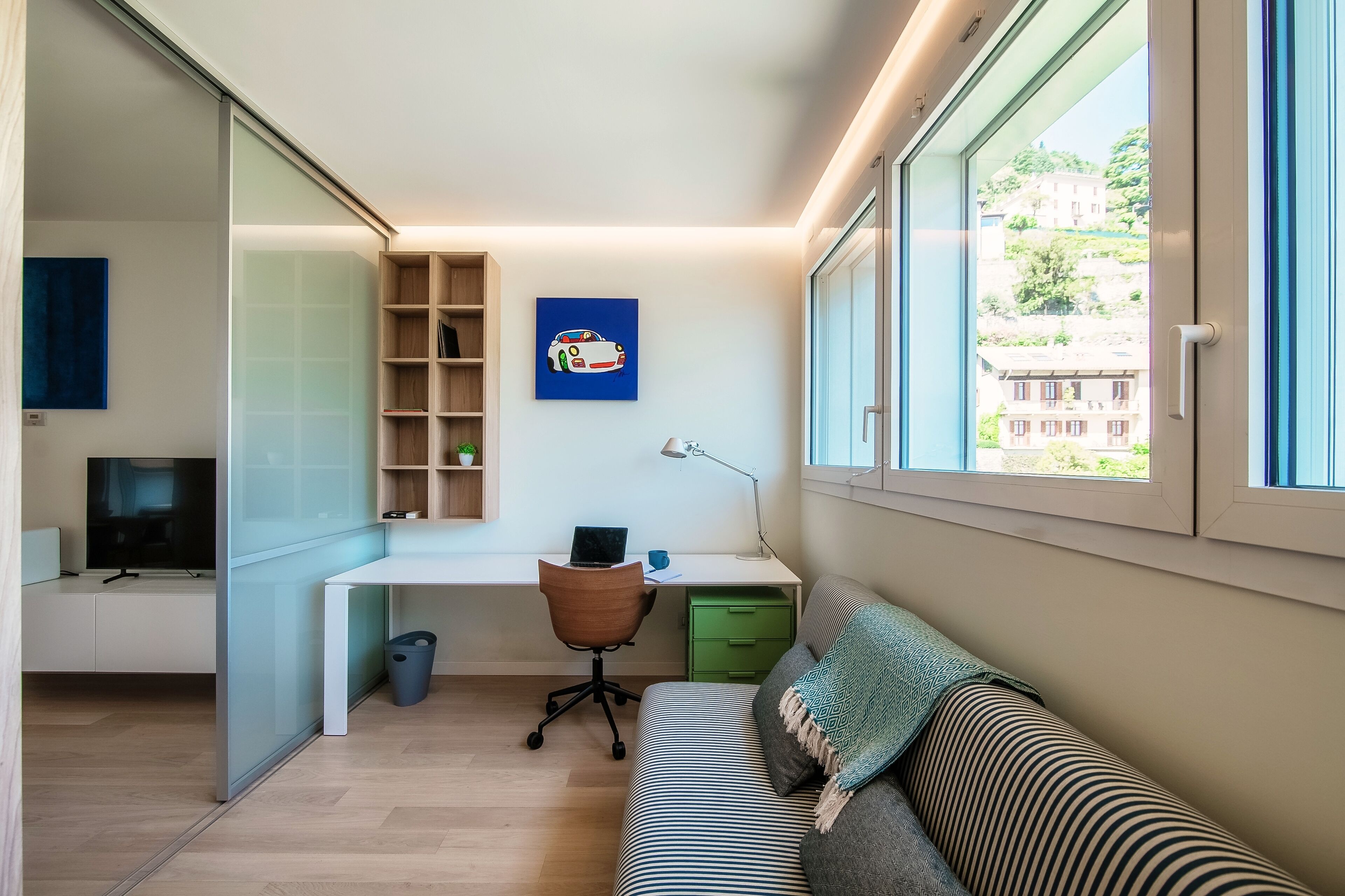 Una habitación moderna con escritorio, silla y sofá. Se ve una ventana con vista a edificios.