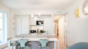 Una cocina moderna con una isla central, armarios blancos y un comedor con dos sillas.