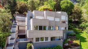Una casa moderna de varios pisos con techo plano, ventanas amplias y un jardín cuidado.
