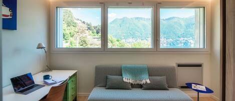 A modern room with a desk, laptop, and a green chair. There is a striped sofa with a blanket and a view of mountains through large windows.