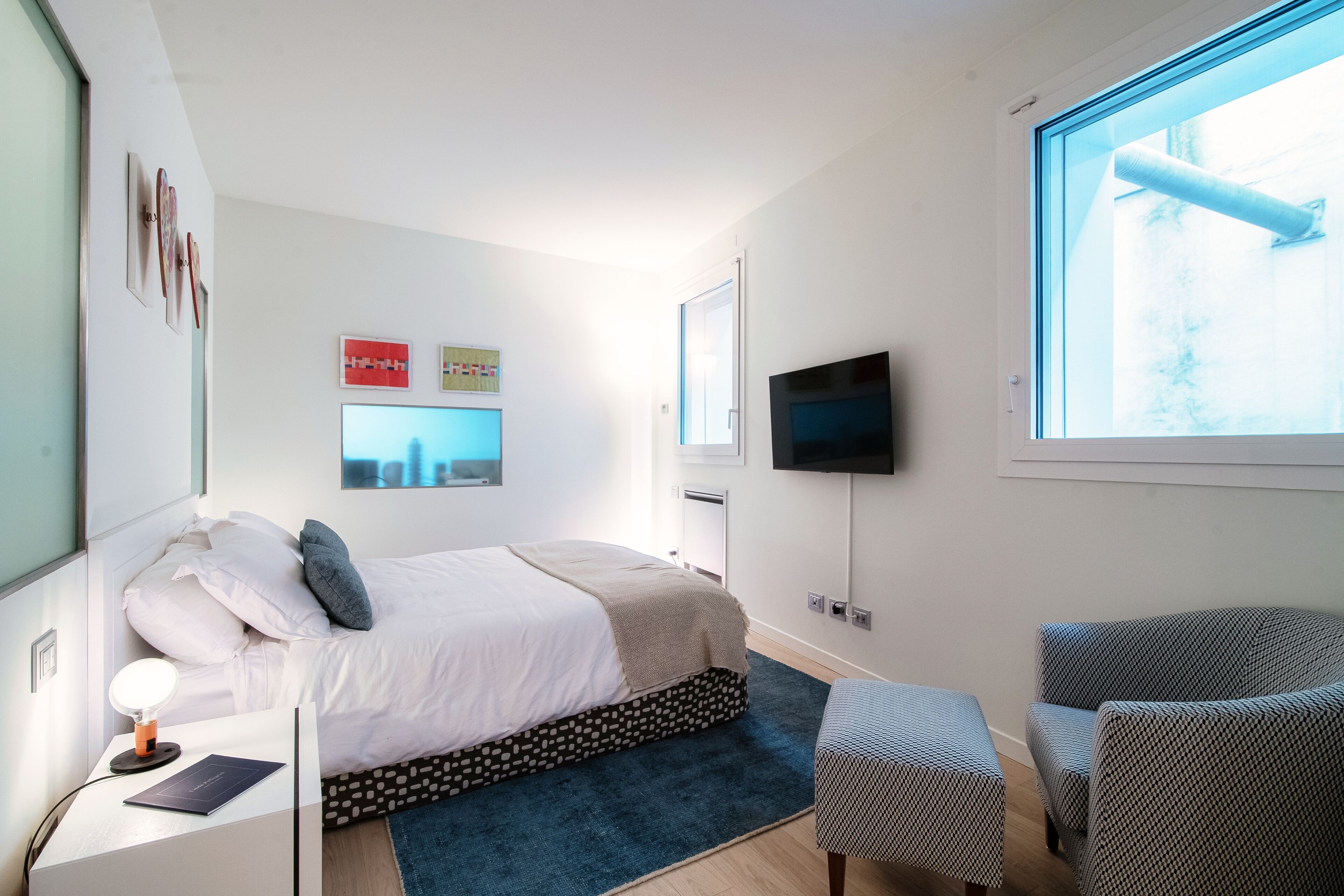 Ein modernes Schlafzimmer mit Bett, Nachttisch, Sessel, Fernseher und Kunstwerk an der Wand.