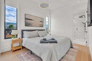 Une chambre à coucher moderne avec un grand lit, une vue sur le ciel, un tableau et un espace douche.