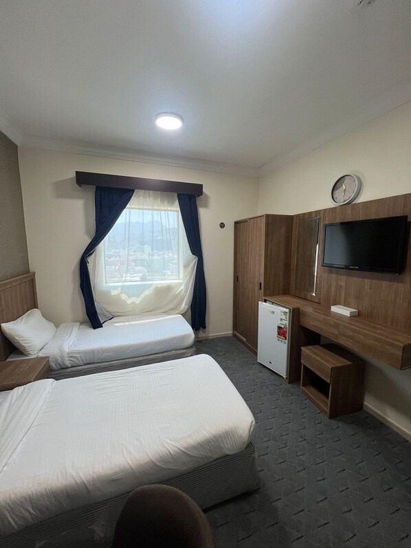 A hotel room with two beds, a small refrigerator, a TV, and a window with curtains.