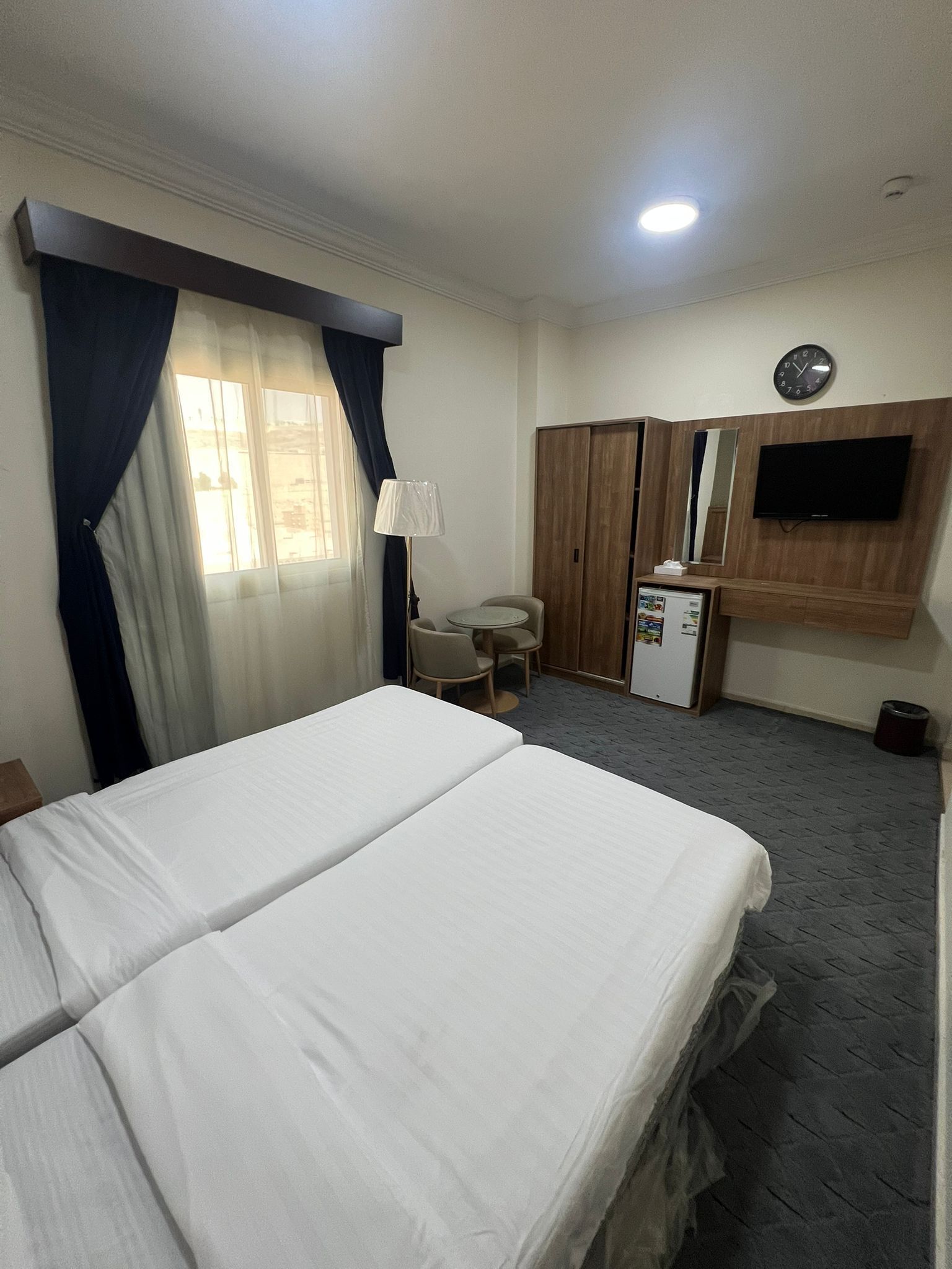 A hotel room with two beds, a desk, a chair, a TV, and a wardrobe.