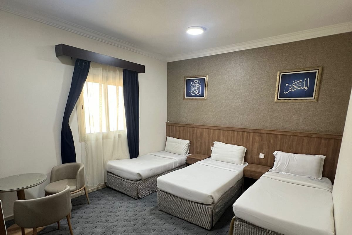 Ein Hotelzimmer mit zwei Einzelbetten, einem kleinen Tisch, zwei Stühlen und einem Schreibtisch.