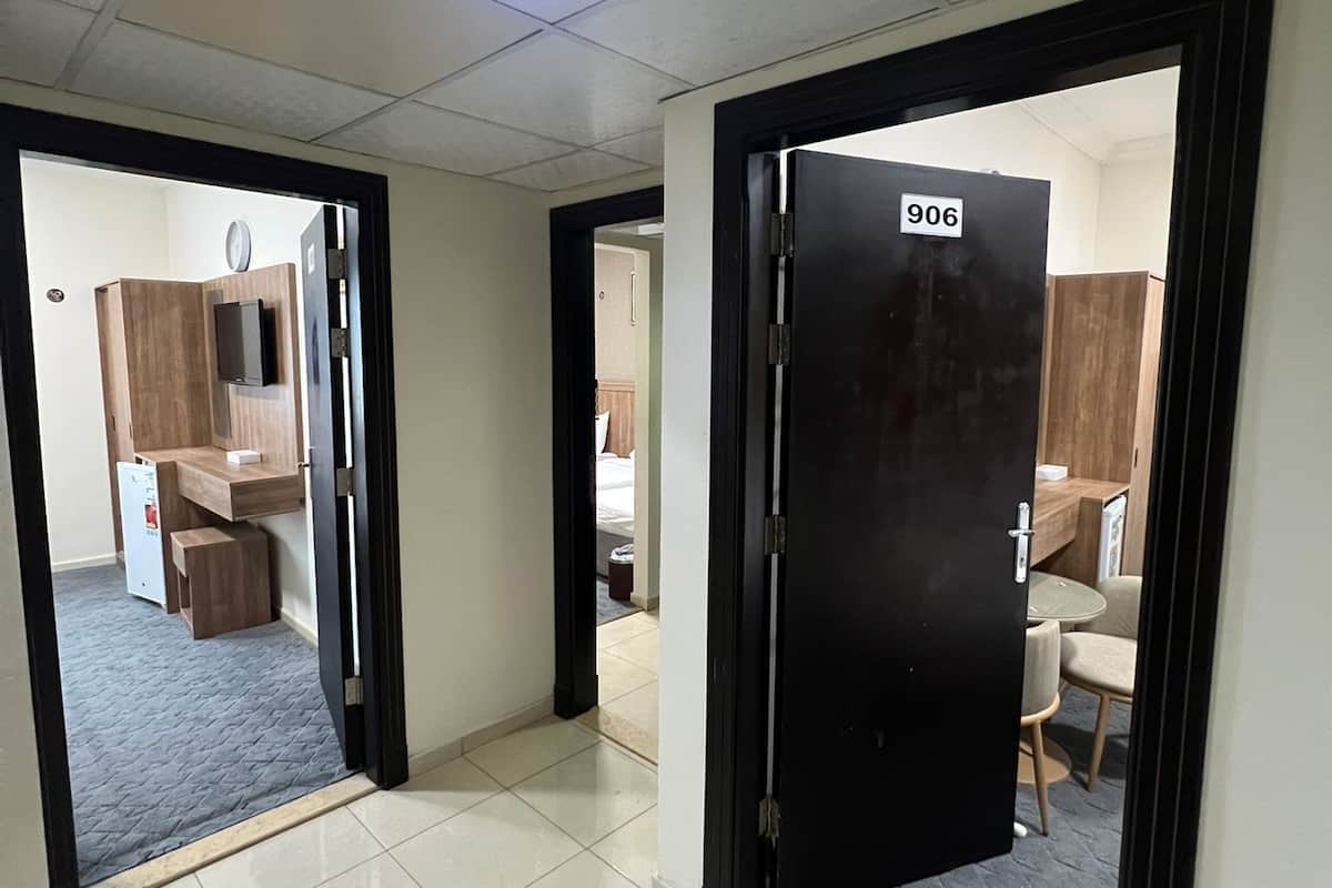 Ein Hotelkorridor mit Fliesenboden, einer schwarzen Tür mit der Bezeichnung '906' und einer Küchenzeile mit Kühlschrank und Mikrowelle.