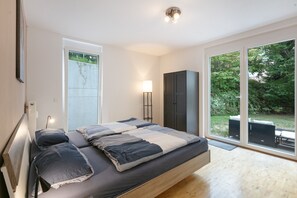 A modern bedroom with a large bed, a wardrobe, a bedside lamp, and a view of the outdoors.