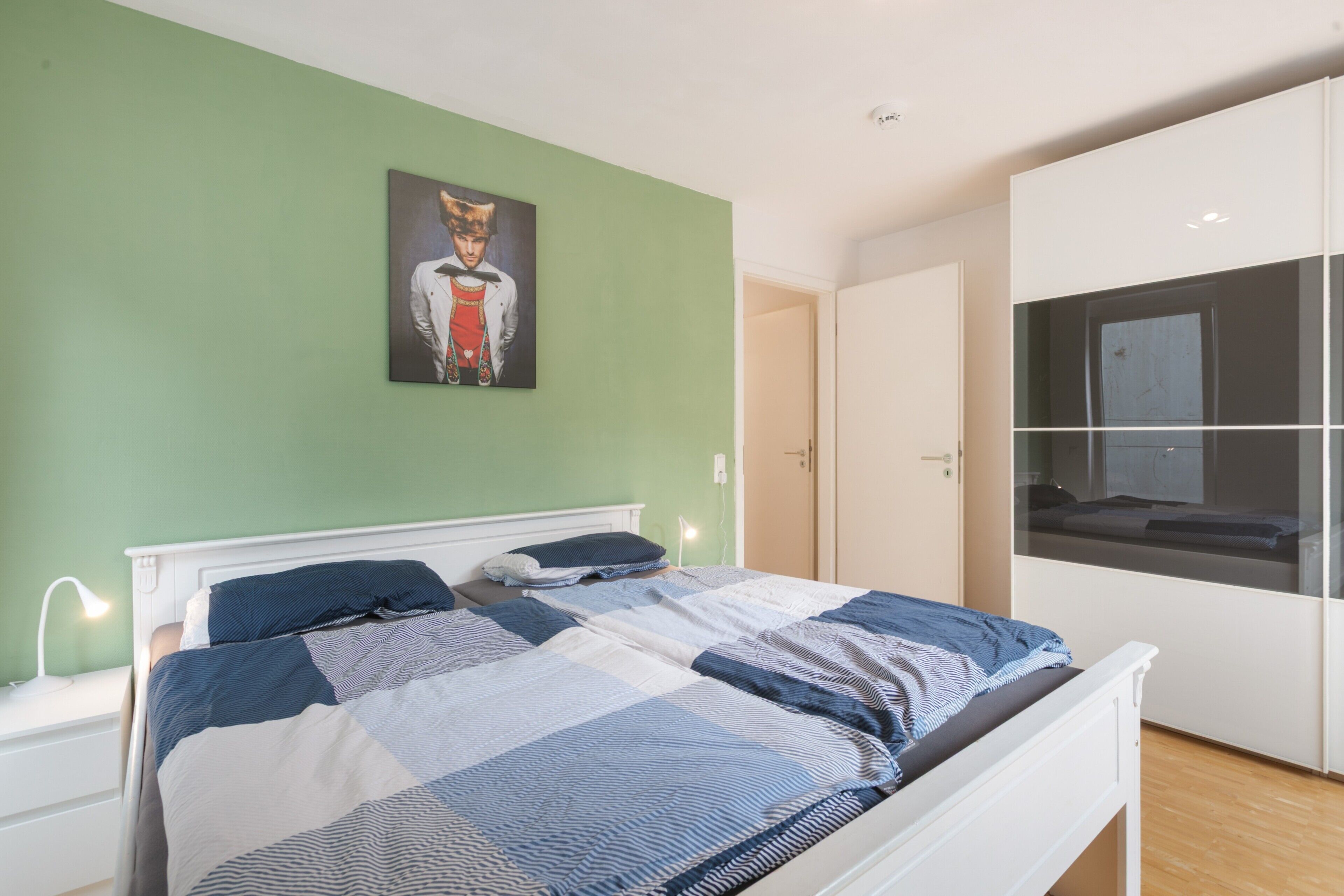 Ein Schlafzimmer mit einem Bett, einem Nachttisch, einer Nachttischlampe, einem Bild an der Wand und einem Kleiderschrank.